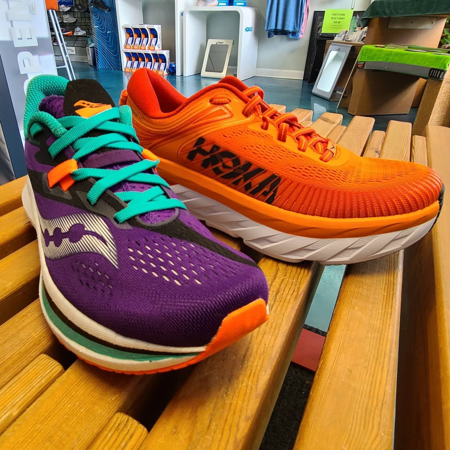 Saucony and Hoka running shoes lined up on a wooden bench inside The Foot Store