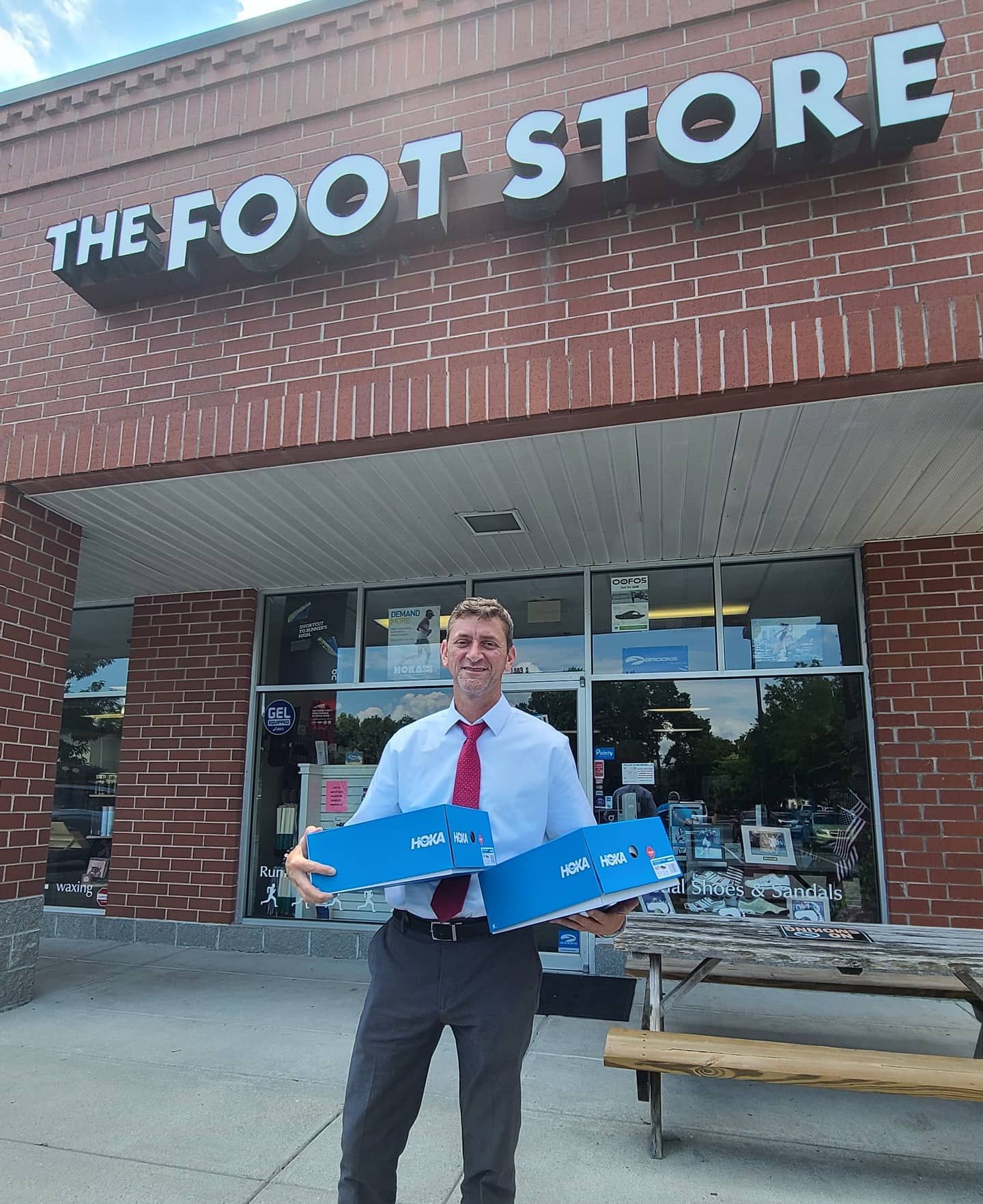 A Foot Store team member outside the Mt. Pleasant storefront holding new Hoka shoe boxes